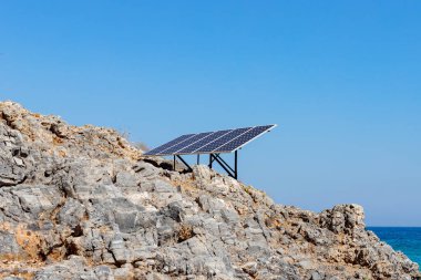 Kayalık deniz kıyısındaki güneş paneli (güneş pili). Alternatif yeşil güneş enerjisinin kaynağı. Doğadaki temiz enerji gücünü kavra. Boşluğu kopyala