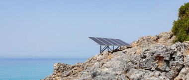 Kayalık deniz kıyısındaki güneş paneli (güneş pili). Alternatif yeşil güneş enerjisinin kaynağı. Doğadaki temiz enerji gücünü kavra. Boşluğu kopyala
