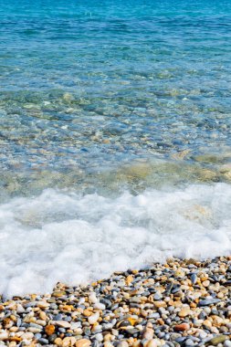 Sahildeki deniz dalgaları. Şeffaf deniz suyu ve çakıl taşları. Yaz tatili için deniz kenarı tatil beldesi