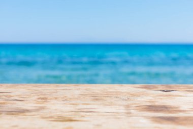 Bulanık mavi denizin üzerindeki ahşap masa. Deniz kıyısında boş ahşap masa ve mavi gökyüzü. Denizde yaz tatili kavramı