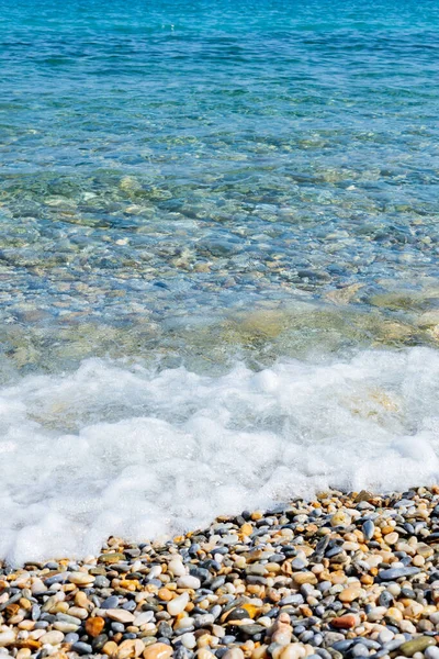Sahildeki deniz dalgaları. Şeffaf deniz suyu ve çakıl taşları. Yaz tatili için deniz kenarı tatil beldesi