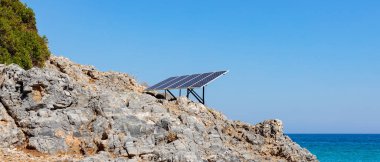 Kayalık deniz kıyısındaki güneş paneli (güneş pili). Alternatif yeşil güneş enerjisinin kaynağı. Doğadaki temiz enerji gücünü kavra. Boşluğu kopyala