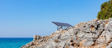 Kayalık deniz kıyısındaki güneş paneli (güneş pili). Alternatif yeşil güneş enerjisinin kaynağı. Doğadaki temiz enerji gücünü kavra. Boşluğu kopyala