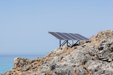 Kayalık deniz kıyısındaki güneş paneli (güneş pili). Alternatif yeşil güneş enerjisinin kaynağı. Doğadaki temiz enerji gücünü kavra. Boşluğu kopyala