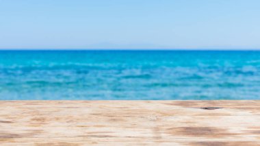 Bulanık mavi denizin üzerindeki ahşap masa. Deniz kıyısında boş ahşap masa ve mavi gökyüzü. Denizde yaz tatili kavramı