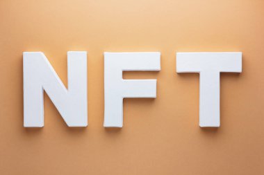 Para iadesi olmayan jeton. Bej arkaplandaki beyaz harflerden yapılmış NFT yazıtları. Toprak rengi arkaplan üzerinde NFT 3D metin. Kriptoart ve engelleme teknolojisi kavramı