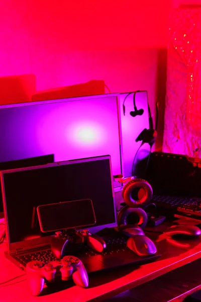 游戏玩家的工作空间 桌面上有游戏机 电脑鼠标 键盘和笔记本电脑 霓虹灯下的游戏配件和计算机设备 赌博成瘾概念 — 图库照片