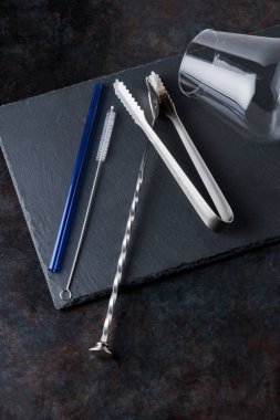 Kokteyl yapma araçları ve tahta üzerinde cam. Bar aletleri: Kokteyl kaşığı, buz maşası, arka planda kamış. Kokteyl aletleri