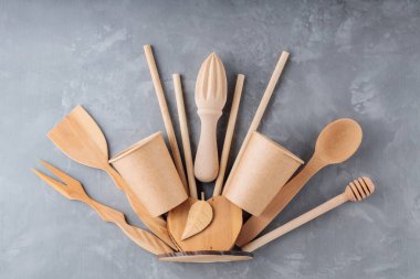Gri arka planda yeniden kullanılabilir ahşap mutfak aletleri. Ahşap mutfak gereçleri, bambu pipetleri ve betonun üzerinde tek kullanımlık kağıt bardaklar. Sürdürülebilir yaşam tarzı. Plastiksiz konsept