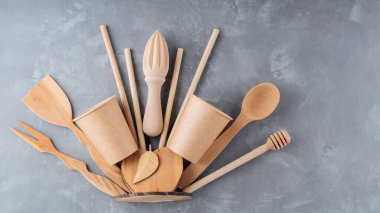 Gri arka planda yeniden kullanılabilir ahşap mutfak aletleri. Ahşap mutfak gereçleri, bambu pipetleri ve betonun üzerinde tek kullanımlık kağıt bardaklar. Sürdürülebilir yaşam tarzı. Plastiksiz konsept