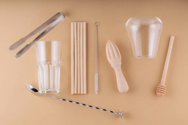 Kokteyl kaşığı, buz maşası ve yaz içeceği için bardak. Bambu pipetleri, temizlik fırçası ve bej arka planda ahşap sıkacağı. Sıfır atık, geri dönüşüm, sürdürülebilir yaşam tarzı kavramı