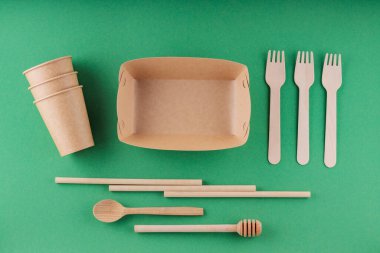 Çevre dostu sofra takımı, tek kullanımlık kağıt bardak ve yeşil arka planda ahşap çatal bıçak takımı. Çevre dostu tek kullanımlık sofra takımı, bambu pipetleri ve çatallar. Plastiksiz konsept