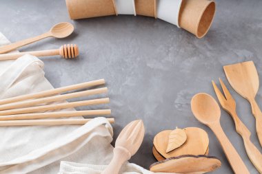 Ahşap masa takımı, kağıt bardaklar ve gri arka planda keten alışveriş torbası. Sıfır atık seti, ağ torbası, bambu kamışları ve ahşap çatal bıçaklar. Çevre dostu kavram