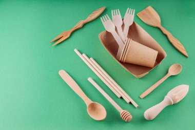 Kağıtlar biyolojik olarak çözünebilir sofra takımı ve yeşil arka planda ahşap çatal bıçak takımı. Çevre dostu mutfak aletleri, bambu çatalları, karton kaplar ve bardaklar. Sürdürülebilir yaşam tarzı. Boşluğu kopyala