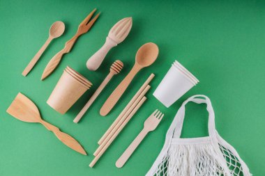 Çevre dostu mutfak aletleri ve yeşil arka planda örgü. Ahşap çatal bıçak takımı, kağıt, ayrıştırılabilir sofra takımı ve alışveriş çantası. Sıfır atık. Üst görünüm