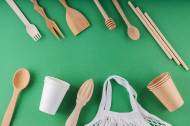 Çevre dostu mutfak aletleri ve yeşil arka planda örgü. Ahşap çatal bıçak takımı, kağıt, ayrıştırılabilir sofra takımı ve alışveriş çantası. Sıfır atık. Üst görünüm