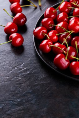 Siyah bir tabakta olgun kiraz. Karanlık bir arka planda tatlı kirazlar. Sağlıklı yaz yemekleri konsepti. Boşluğu kopyala