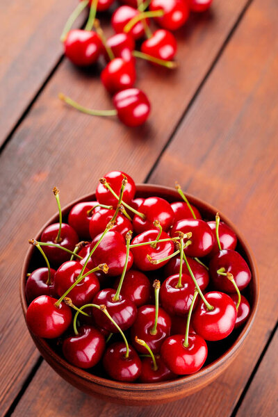 Ripe cherries in a clay bowl. Red cherries on a wooden table. Healthy vegan food concept. Top view. Copy space