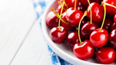 Beyaz tabakta kırmızı kiraz. Tahta bir masada olgun kirazlar. Diyet yemek için kırmızı böğürtlen. Yakın plan.