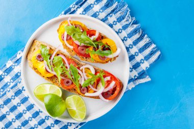 Mavi arka planda geleneksel İspanyol tapaları. Sebzeli, yeşillikli, zeytinli ve limonlu sağlıklı sandviçler. Beyaz tabakta vejetaryen sandviçler. Üst görünüm