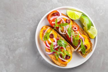 Sağlıklı vejetaryen tostları ve beyaz tabakta limon. Domatesli, yeşillikli ve zeytinli Sağlıklı açık sandviçler. Üst Manzara. Boşluğu kopyala