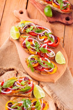 Kesme tahtasındaki İspanyol mezeleri ve limon. Domatesli, yeşillikli ve zeytinli Tahta tahtada sağlıklı açık sandviçler. Üst görünüm