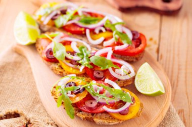 Kesme tahtasındaki İspanyol mezeleri ve limon. Domatesli, yeşillikli ve zeytinli Tahta tahtada sağlıklı açık sandviçler. Üst görünüm