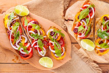 Kesme tahtasındaki İspanyol mezeleri ve limon. Domatesli, yeşillikli ve zeytinli Tahta tahtada sağlıklı açık sandviçler. Üst görünüm