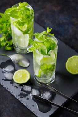Mojito kokteyli, limon dilimleri, arka planda nane ve buz. Kokteyl mojito, buz maşası ve kokteyl kaşığı. Üst görünüm