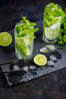 Mojito kokteyli, limon dilimleri, arka planda nane ve buz. Kokteyl mojito, buz maşası ve kokteyl kaşığı. Üst görünüm