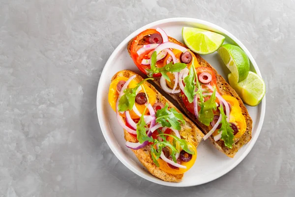 Sağlıklı vejetaryen tostları ve beyaz tabakta limon. Domatesli, yeşillikli ve zeytinli Sağlıklı açık sandviçler. Üst Manzara. Boşluğu kopyala