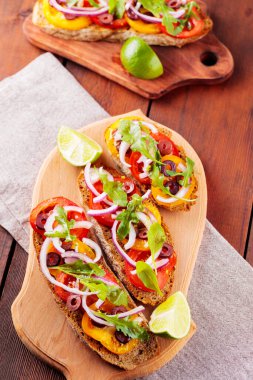 Kesme tahtasında sağlıklı vejetaryen tapas ve limon. Domatesli, yeşillikli ve zeytinli vejetaryen tostları. Tahta tahtalarda sandviçleri aç. Üst görünüm