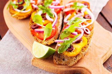 Kesme tahtasında sağlıklı vejetaryen tapas ve limon. Domatesli, yeşillikli ve zeytinli vejetaryen tostları. Tahta tahtalarda sandviçleri aç. Üst görünüm
