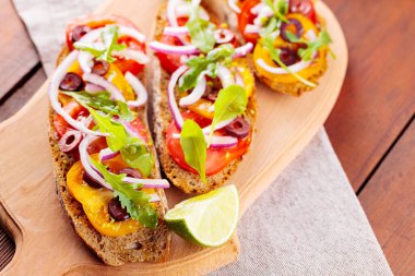 Kesme tahtasında sağlıklı vejetaryen tapas ve limon. Domatesli, yeşillikli ve zeytinli vejetaryen tostları. Tahta tahtalarda sandviçleri aç. Üst görünüm