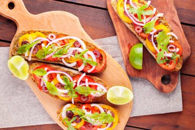Kesme tahtasında sağlıklı vejetaryen tapas ve limon. Domatesli, yeşillikli ve zeytinli vejetaryen tostları. Tahta tahtalarda sandviçleri aç. Üst görünüm
