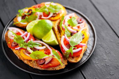 Sağlıklı vejetaryen tostları ve siyah tabakta limon. Domatesli, yeşillikli ve zeytinli Siyah tahtada sağlıklı açık sandviçler. Uzayı kopyala Üst görünüm