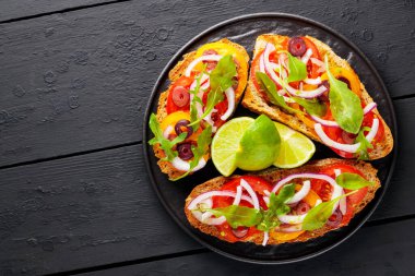 Sağlıklı vejetaryen tostları ve siyah tabakta limon. Domatesli, yeşillikli ve zeytinli Siyah tahtada sağlıklı açık sandviçler. Uzayı kopyala Üst görünüm