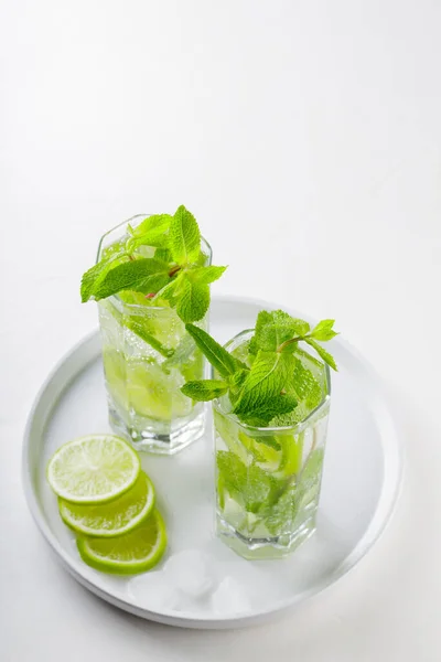 Mojito cocktail on a white background. Two glasses of mojito with mint and lime on a white plate. Summer drink concept. Copy space