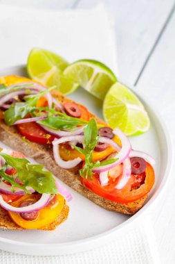Vejetaryen tostları ve beyaz tabakta limon. Domatesli, yeşillikli ve zeytinli Beyaz tahtada sağlıklı açık sandviçler. Sağlıklı vejetaryen tostları.