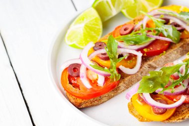 Vejetaryen tostları ve beyaz tabakta limon. Domatesli, yeşillikli ve zeytinli Beyaz tahtada sağlıklı açık sandviçler. Sağlıklı vejetaryen tostları.