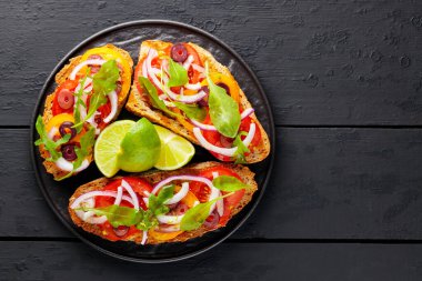 Sağlıklı vejetaryen tostları ve siyah tabakta limon. Domatesli, yeşillikli ve zeytinli Siyah tahtada sağlıklı açık sandviçler. Uzayı kopyala Üst görünüm 