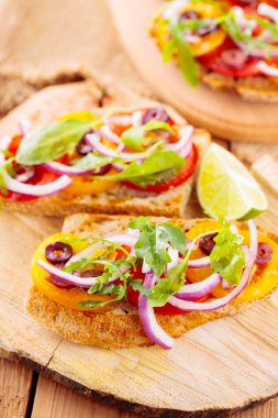 Kesme tahtasındaki İspanyol mezeleri ve limon. Domatesli, yeşillikli ve zeytinli Tahta tahtada sağlıklı açık sandviçler. Üst görünüm