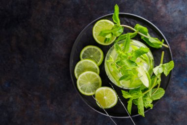Mojito kokteyli, arkaplanda nane ve limon dilimleri. Siyah bir tabakta yaz kokteyli mojito ve buz maşası. Üst Manzara. Boşluğu kopyala