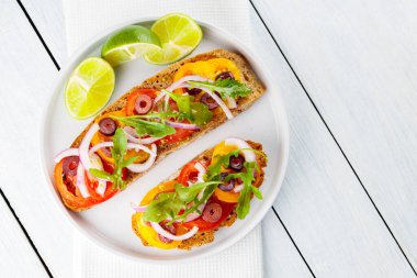 Vejetaryen tostları ve beyaz tabakta limon. Domatesli, yeşillikli ve zeytinli Beyaz tahtada sağlıklı açık sandviçler. Sağlıklı vejetaryen tostları.