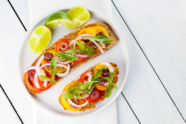 Vejetaryen tostları ve beyaz tabakta limon. Domatesli, yeşillikli ve zeytinli Beyaz tahtada sağlıklı açık sandviçler. Sağlıklı vejetaryen tostları.