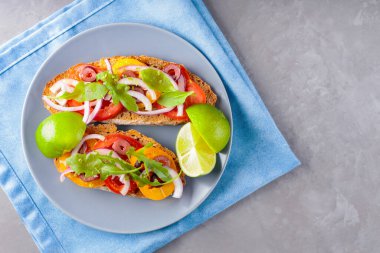 Gri tabakta vejetaryen tostu. Domatesli, yeşillikli ve zeytinli Mavi peçeteli sağlıklı sandviçler. Üst görünüm