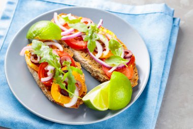 Gri tabakta vejetaryen tostu. Domatesli, yeşillikli ve zeytinli Mavi peçeteli sağlıklı sandviçler. Üst görünüm