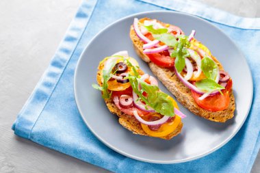 Gri tabakta vejetaryen tostu. Domatesli, yeşillikli ve zeytinli Mavi peçeteli sağlıklı sandviçler. Üst görünüm