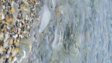 Deniz dalgaları ve çakıl taşları yaklaşıyor. Deniz kıyısına su sıçratıyor. Deniz tatili konsepti. Dikey video