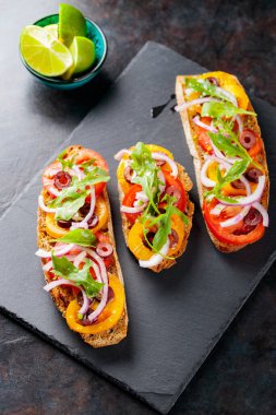 Karanlık bir arka planda İspanyol tapaları. Domates, soğan, yeşillik ve zeytinli vejetaryen tapas. Tahta tahtada sağlıklı sandviçler. Üst görünüm